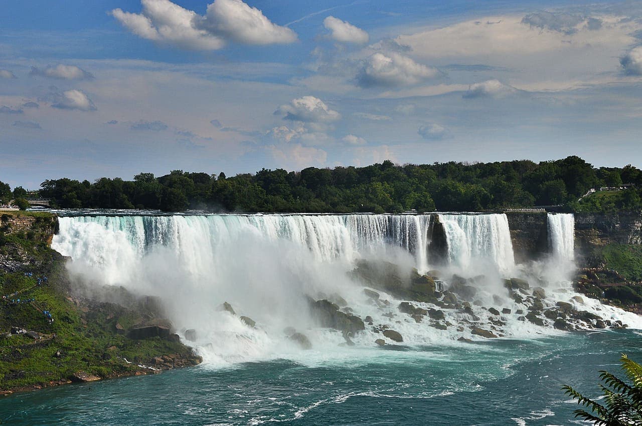 Wide view of Niagara Falls with powerful water cascading over the cliffs and mist rising above the river.