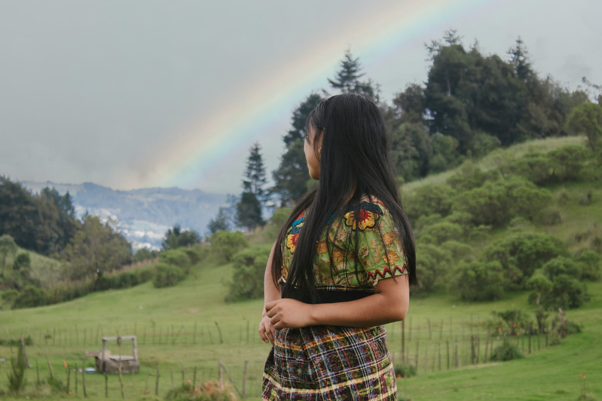Girl in guetemala standing in front of a rainbow in a green landscape