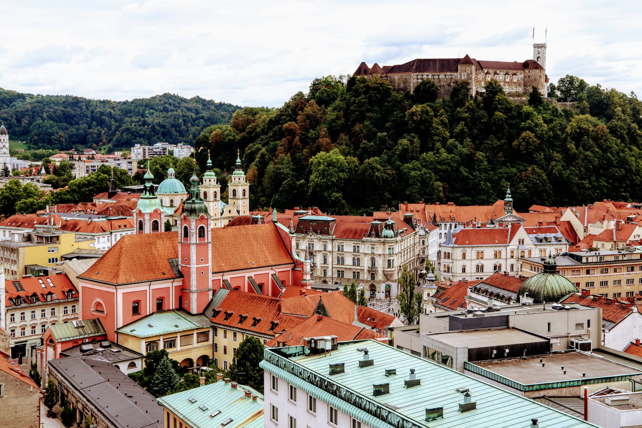 Aerial view of colorful orange roofs in Ljubljana and the green hill with castle in the distance.