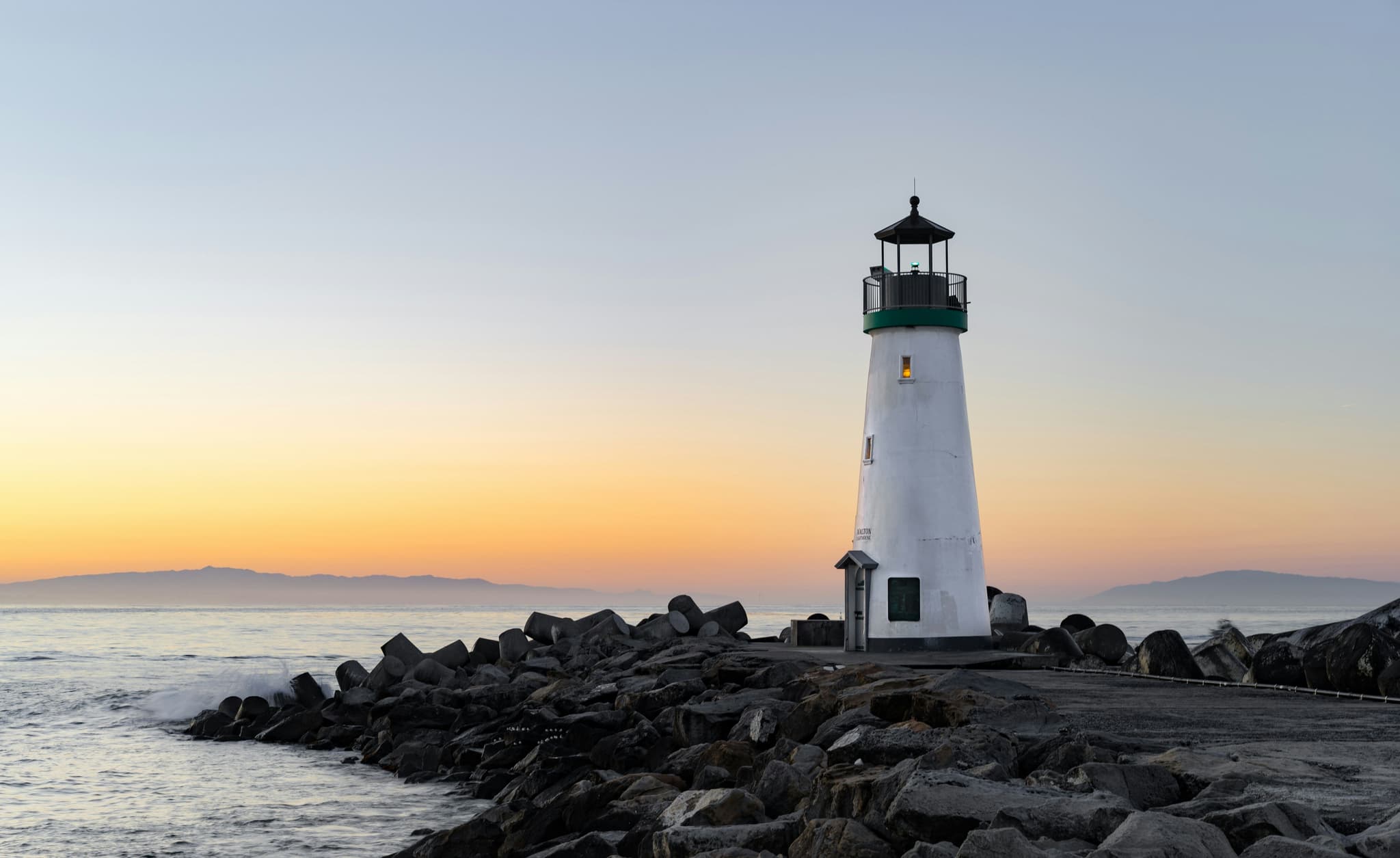The white lighthouse on the rocks by the water during sunset in faro