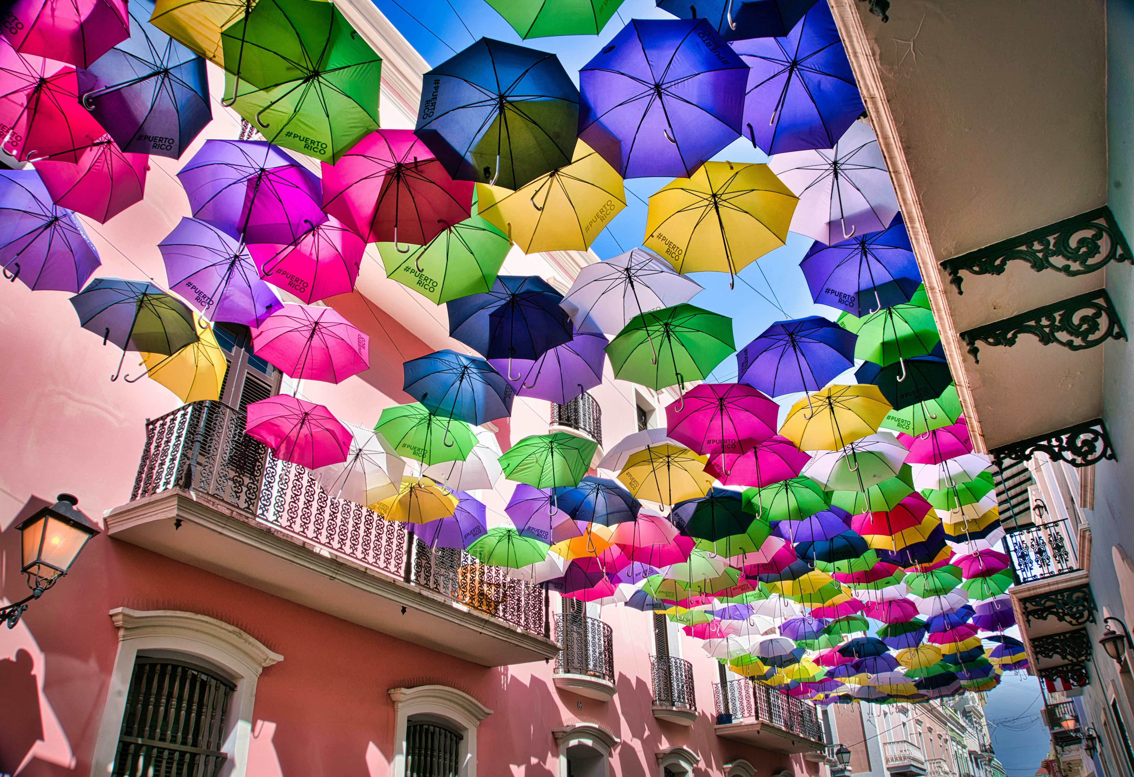 Colourful umbrellas hanging above a street in Antigua Guatemala, creating a vibrant canopy between colonial buildings.