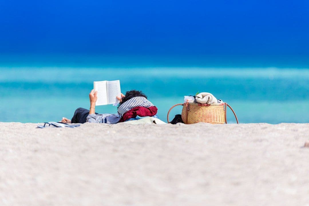 A person reading a book while lying on a beach