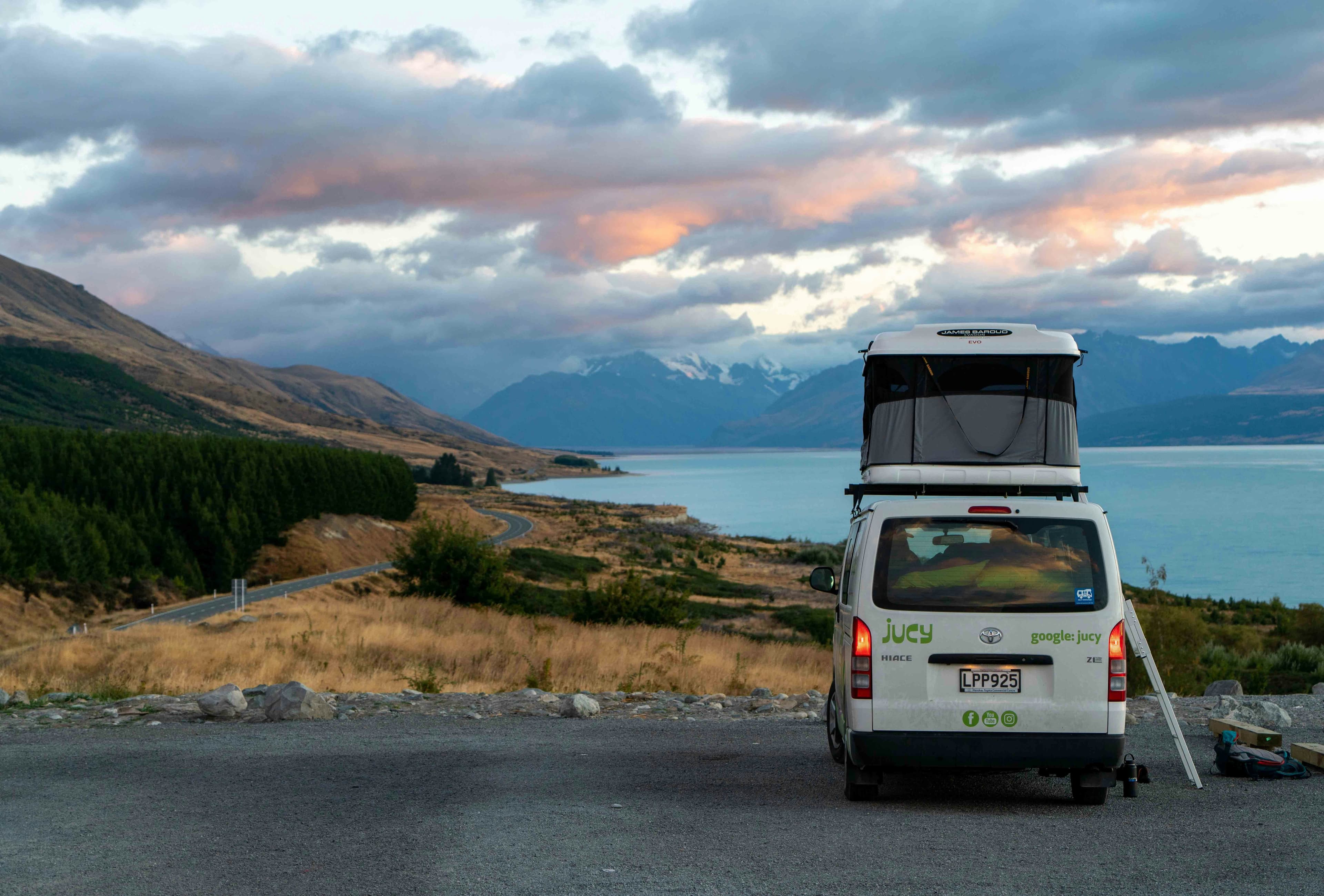 A campervan parked on the road in the mountains of New Zealand next to a lake on a cloudy day