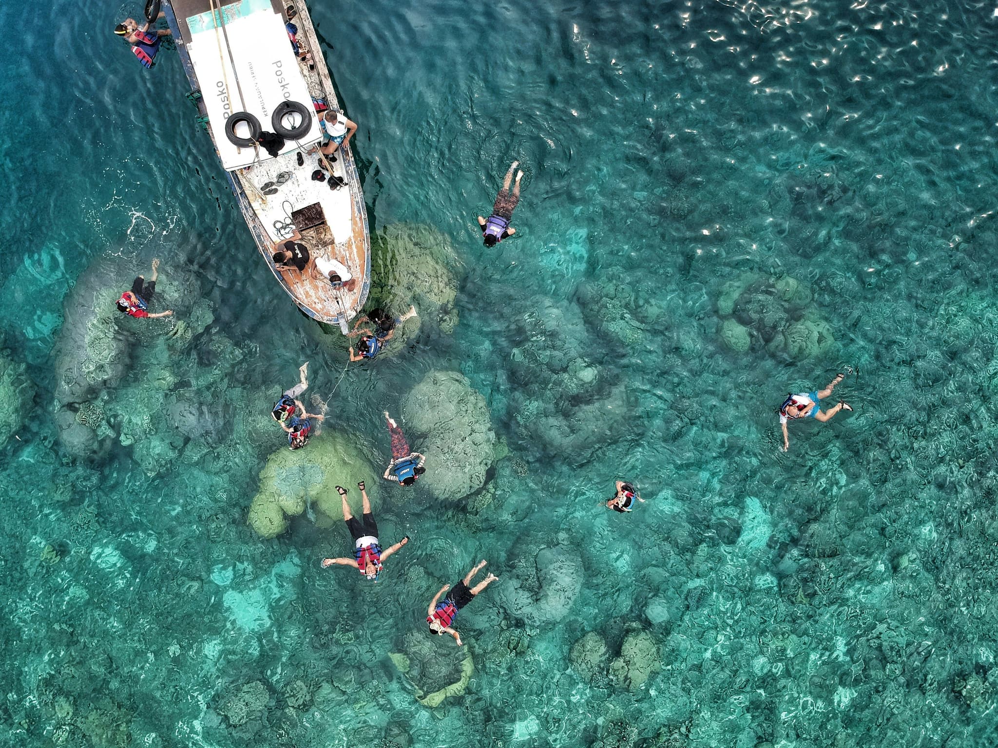 Aerial view of snorkeling people in clear blue water and a boat