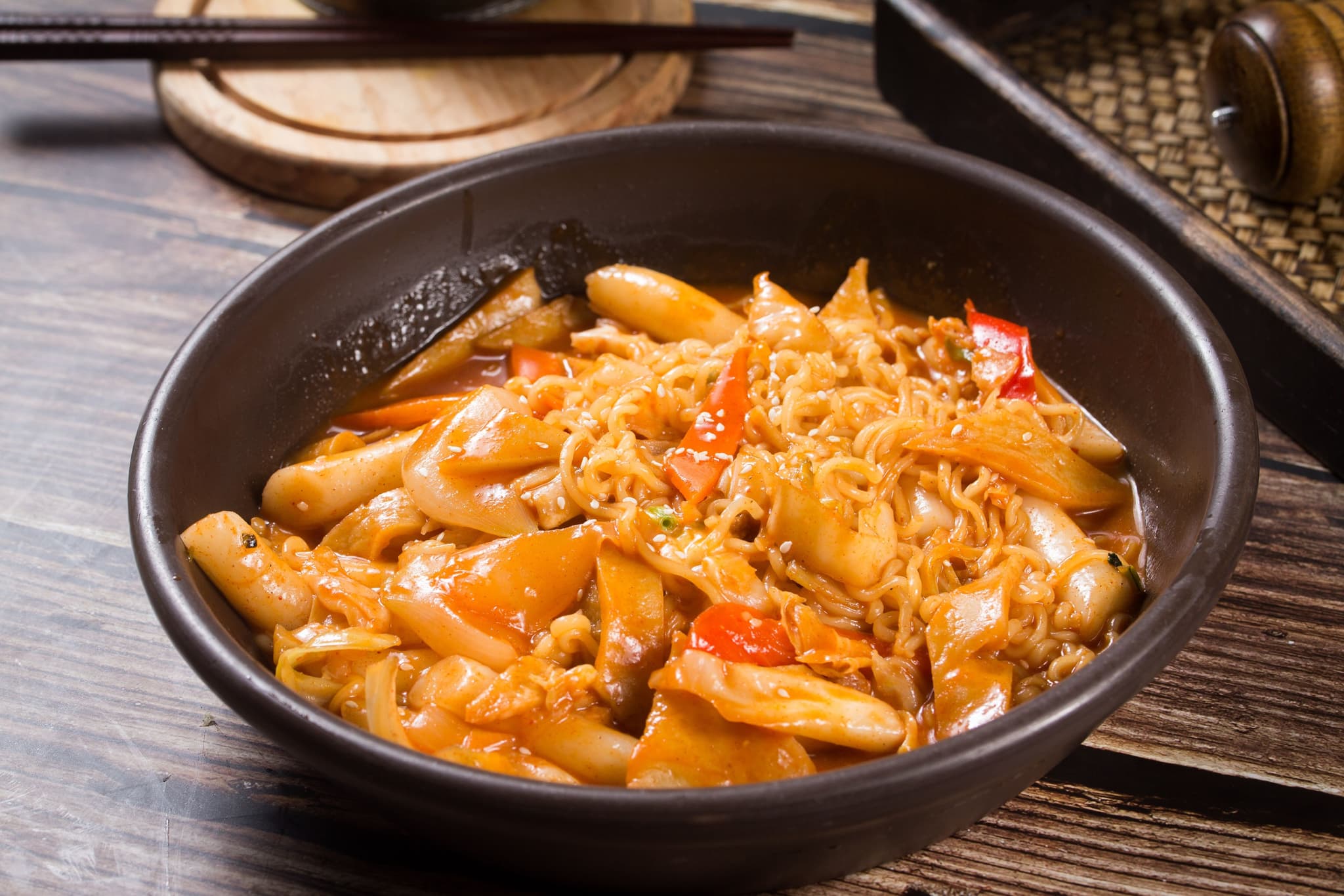 A black bowl with tteokbokki rice cake and orange sauce
