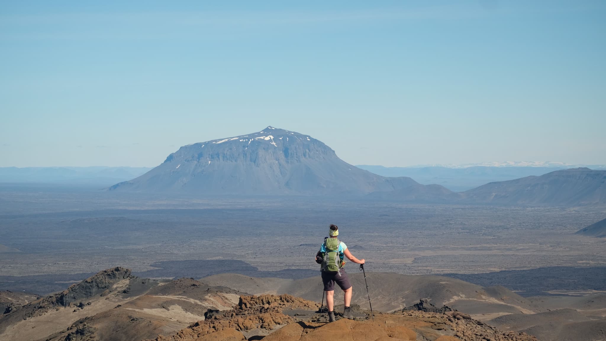 A female hiker standing on a rock looking at a flat topped vulcano mountain in the distance
