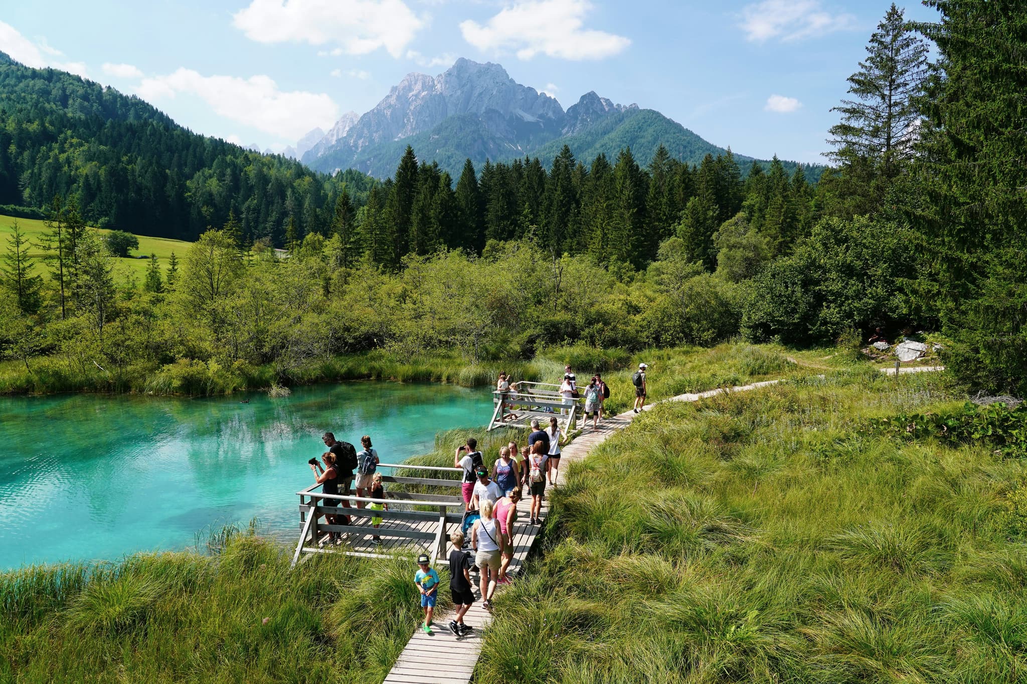 Travellers walking on a path in Kranjska Gora near turqoise lake and surrounded by green nature and mountains