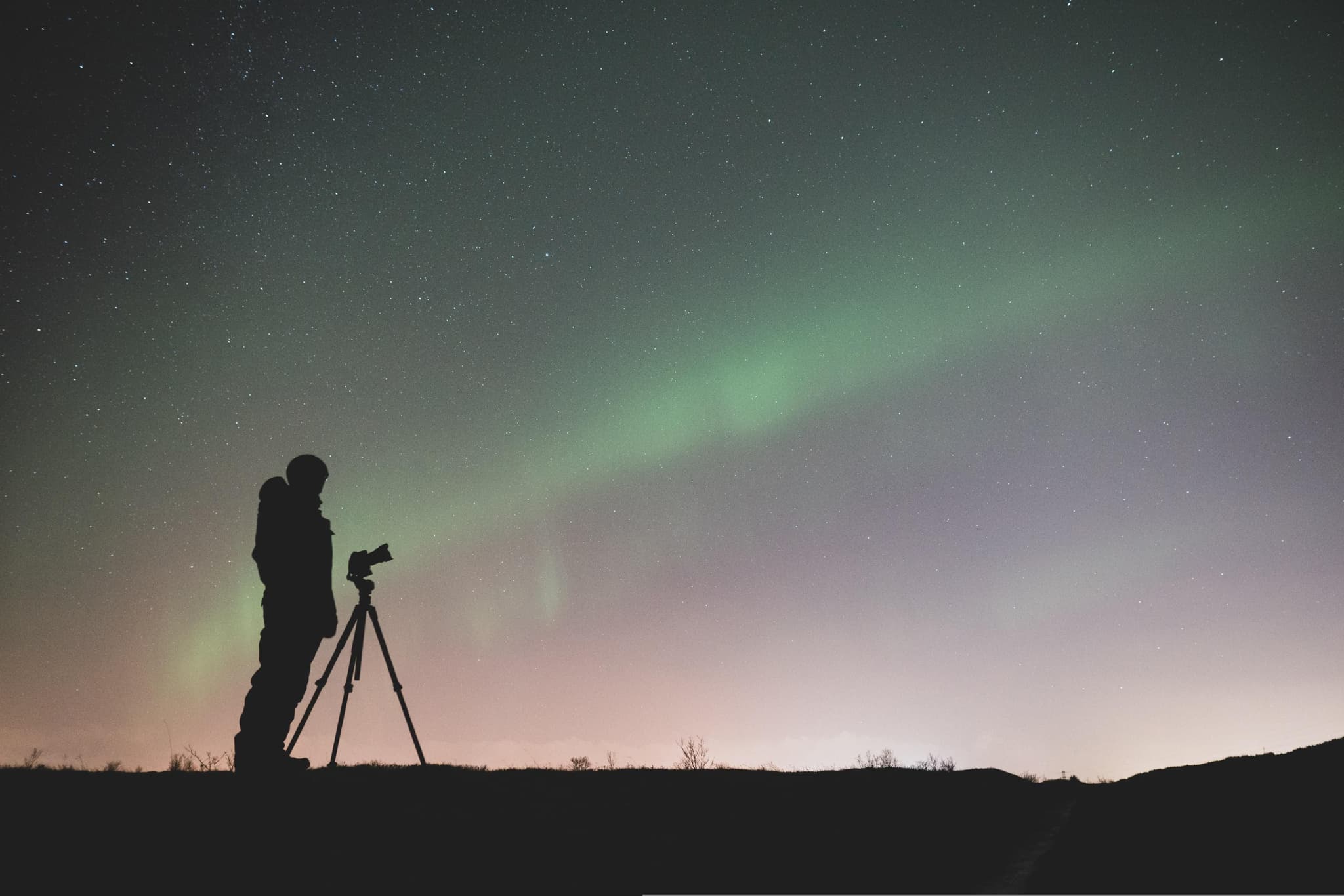 Photographer with a tripod capturing the northern lights in a snowy landscape in Iceland