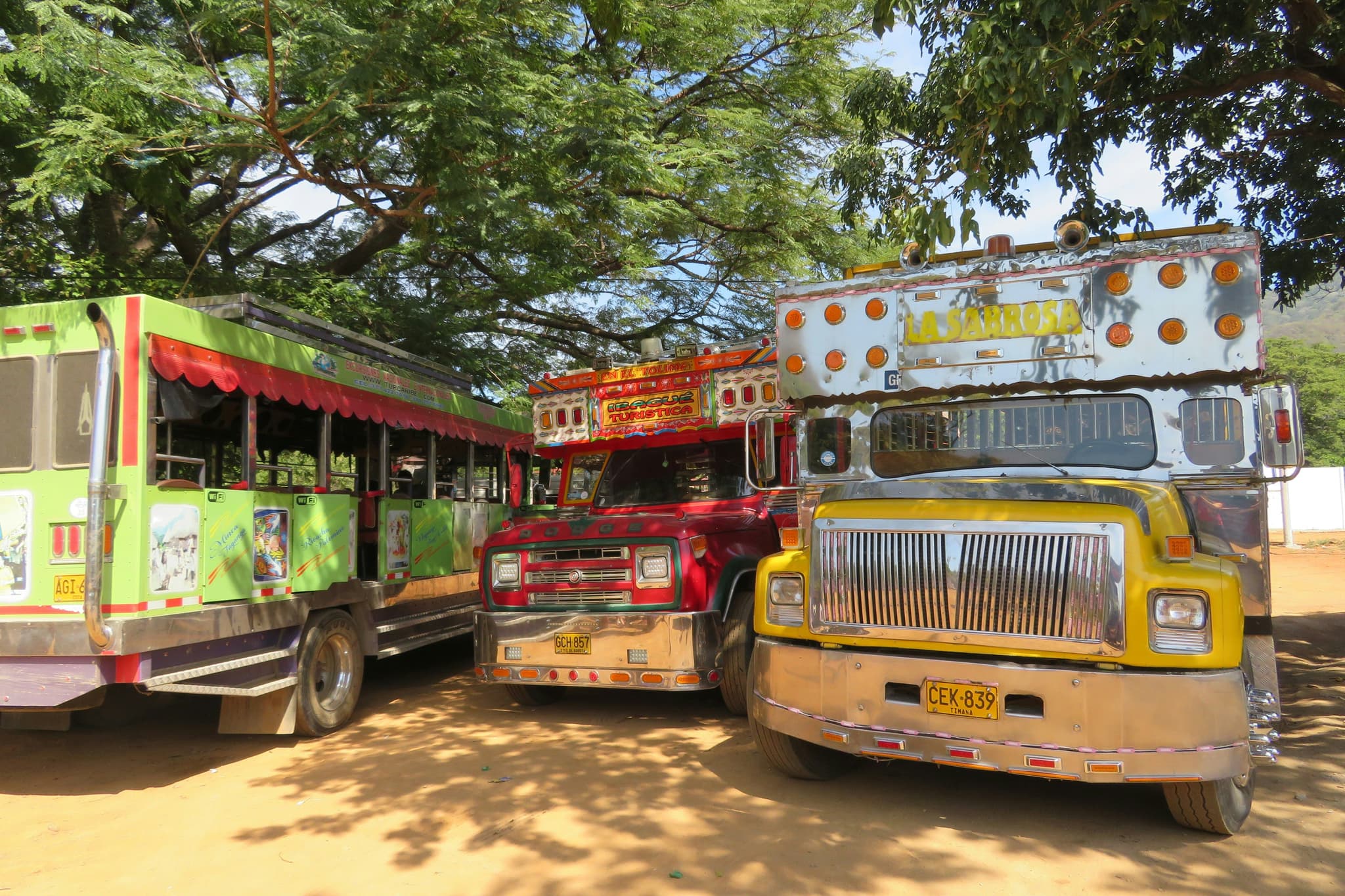 Three colorful local chicken buses on a dirt road