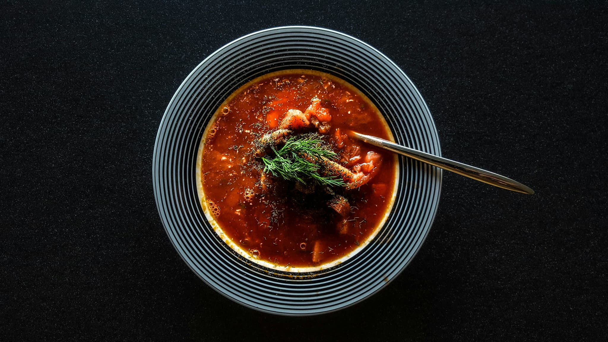 A gray bowl of goulash with black background