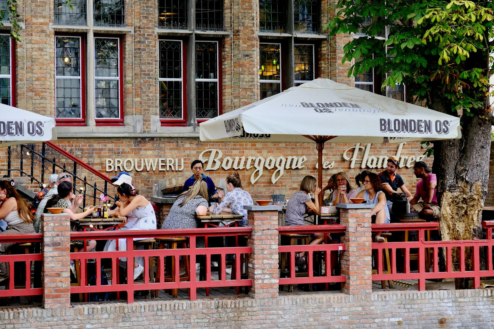 People sitting at tables on a brick café terrace beside a canal in Bruges