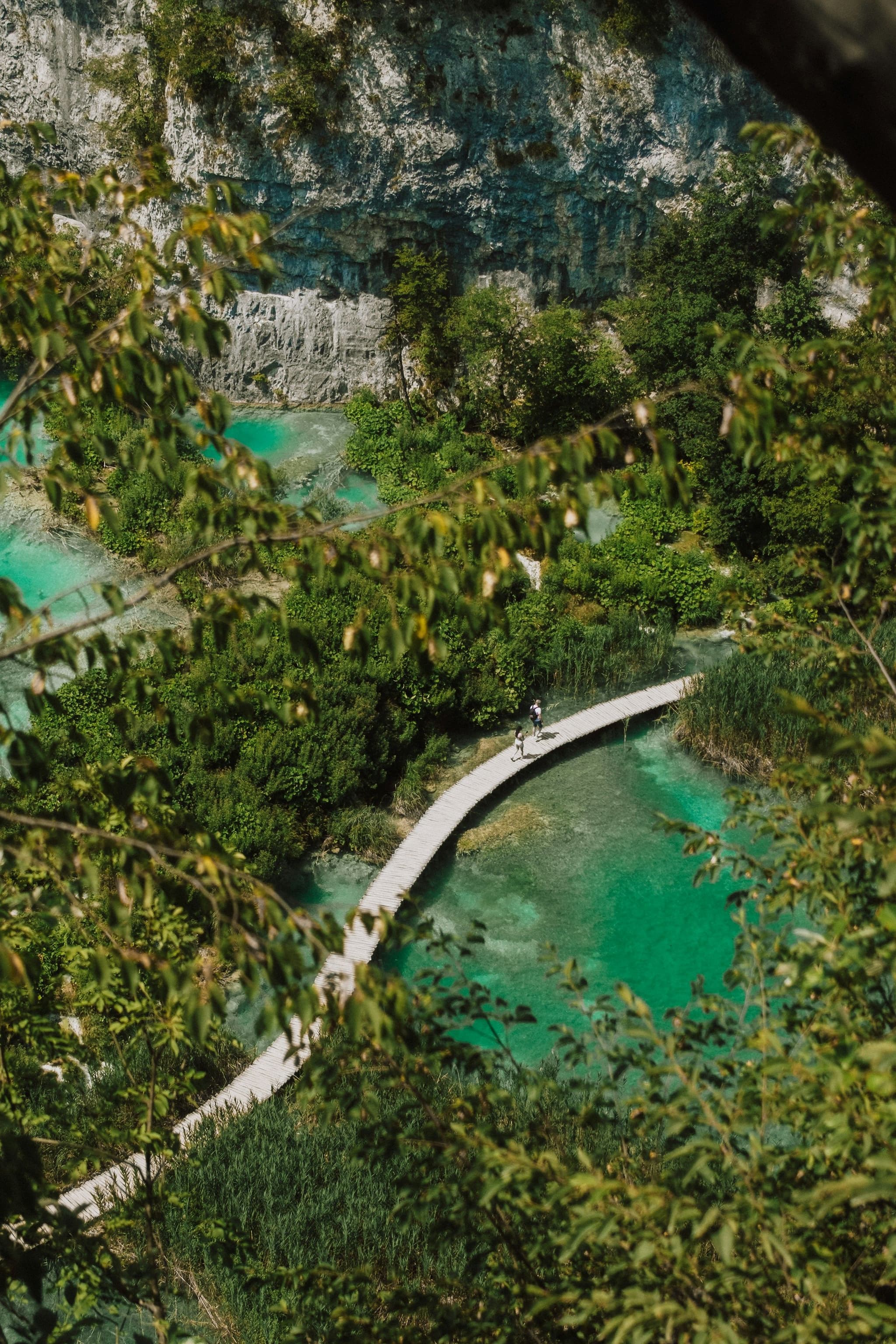 People walking on a wooden boardwalk over turquoise water in Plitvice Lakes National Park