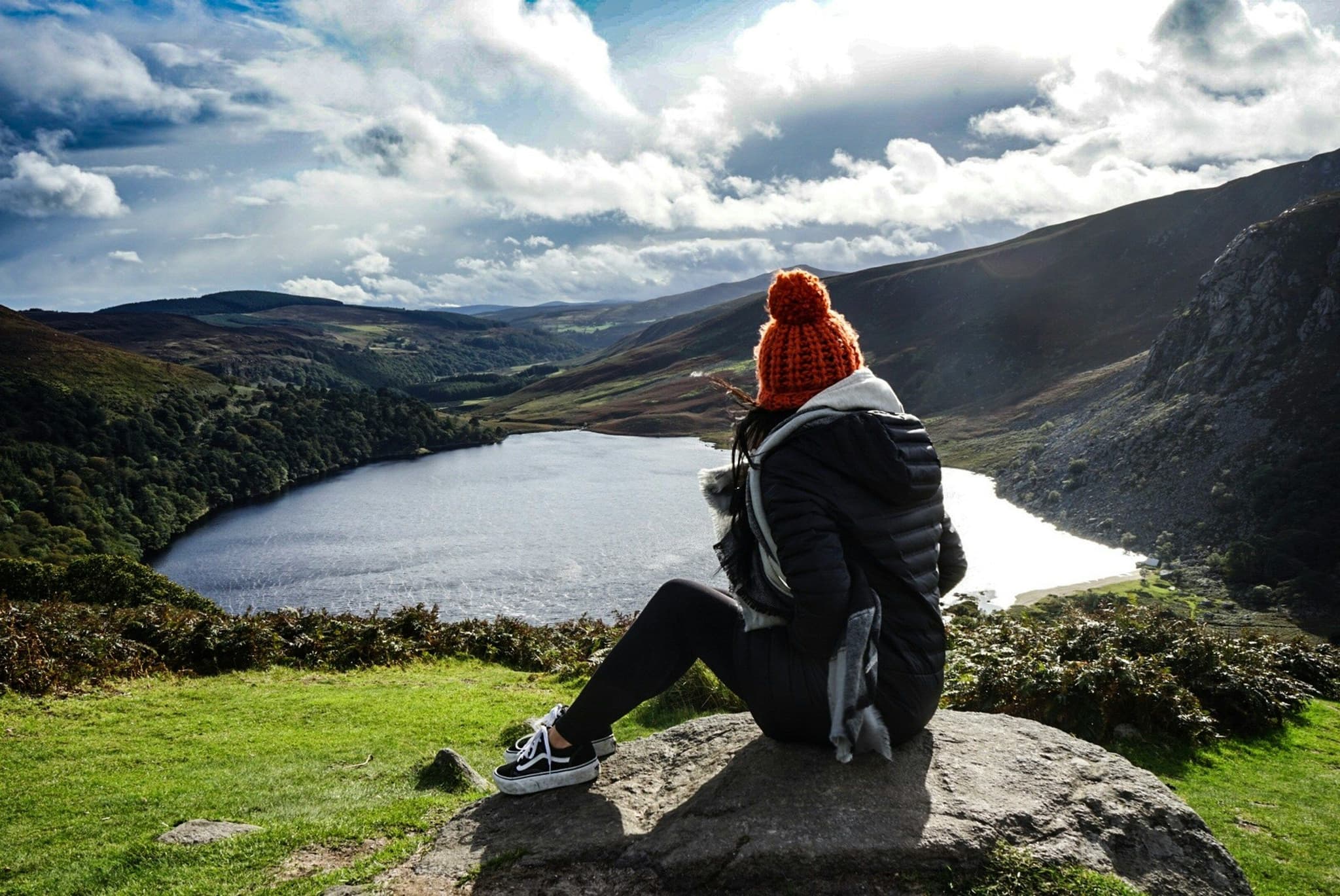 A woman sitting on a viewpoint looking at the lake and mountains in Ireland
