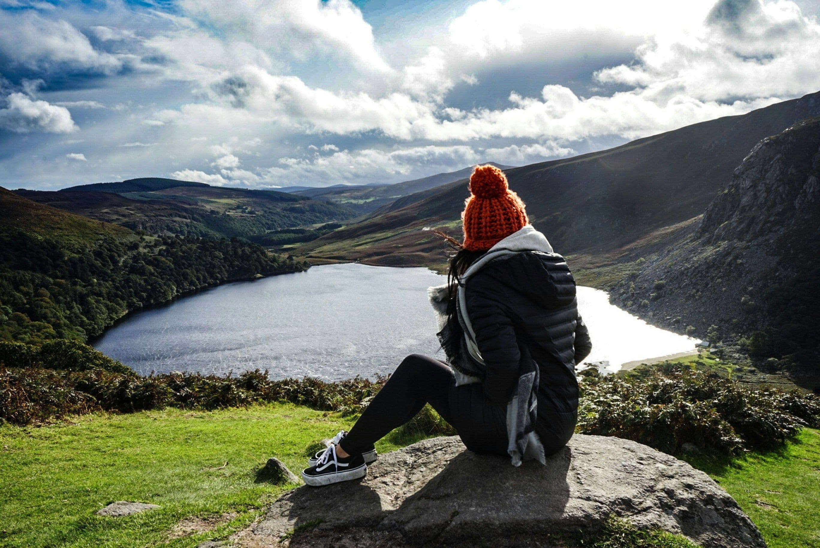 A woman sitting on a viewpoint looking at the lake and mountains in Ireland