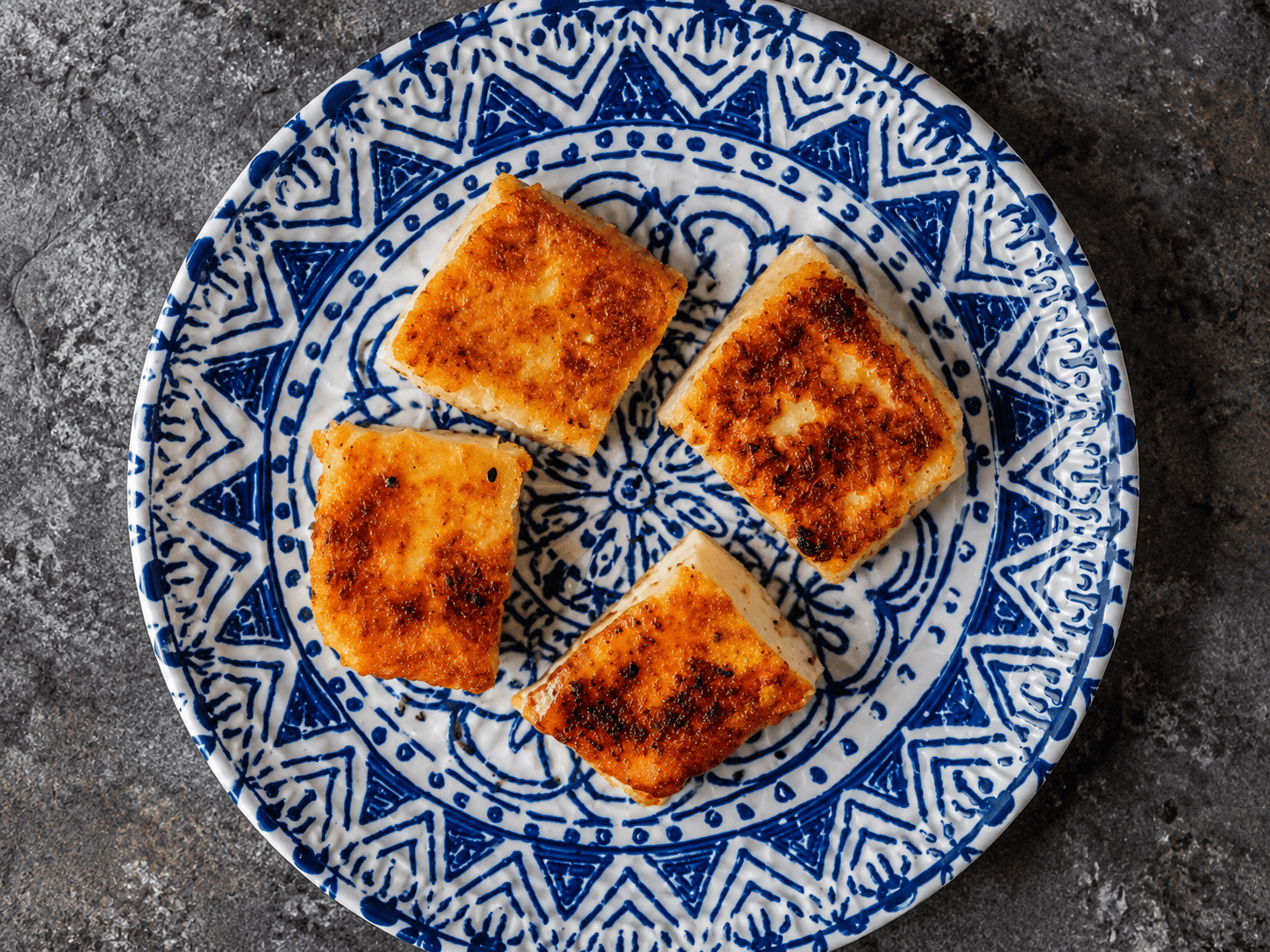Four pieces of Saganaki on a blue and white plate