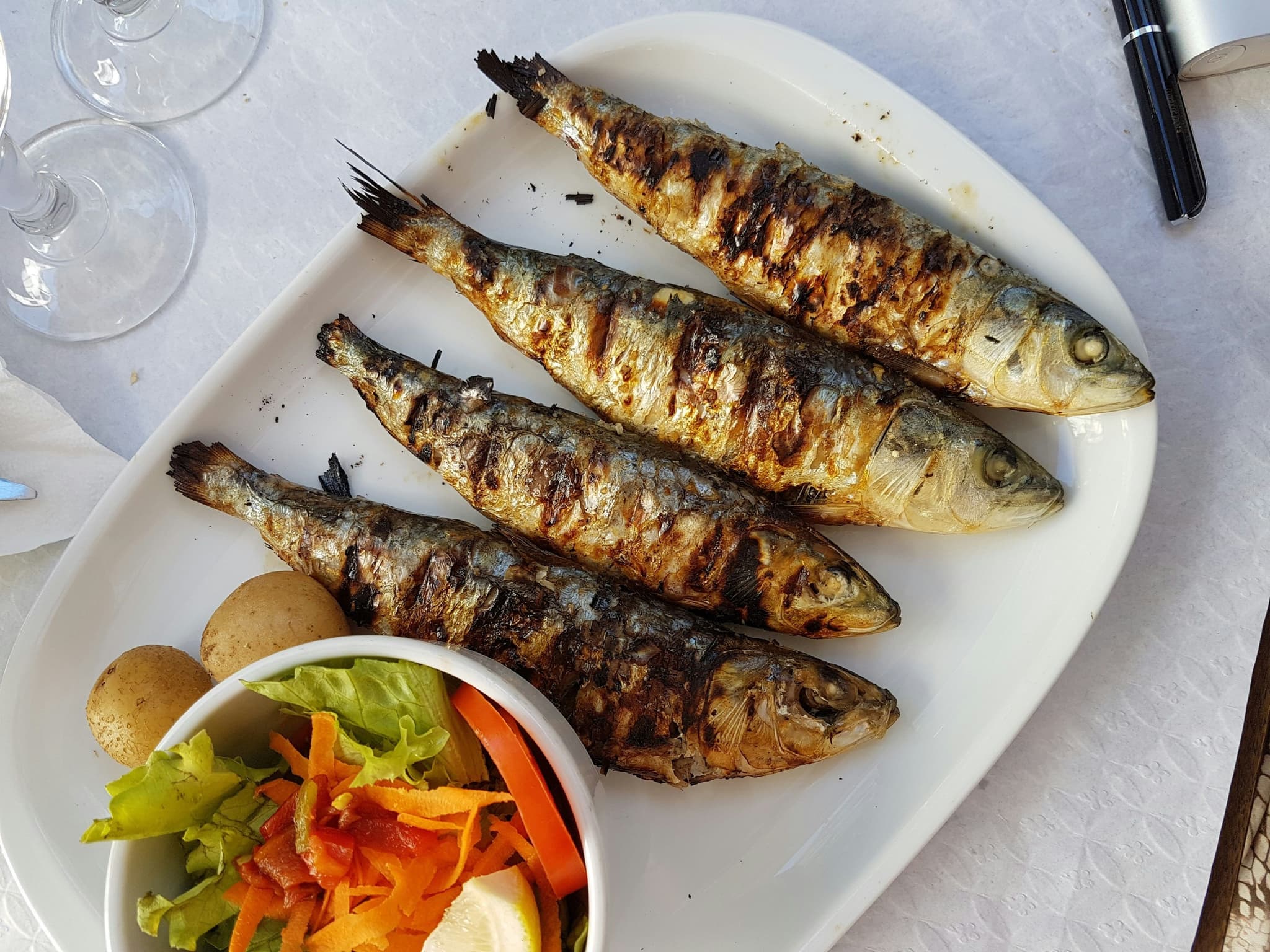 Four sardines on a white plate, and a side salad in a round bowl