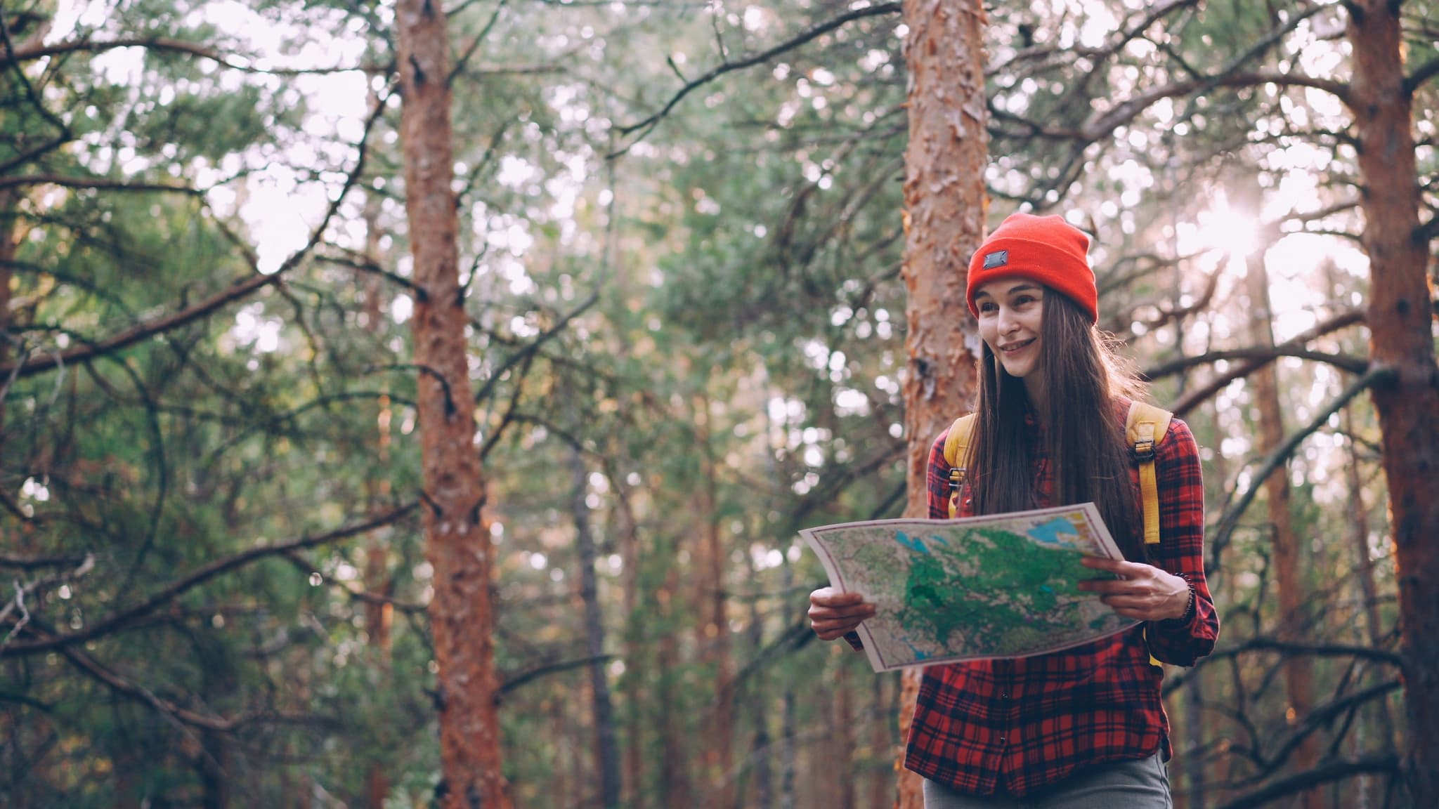 A female solo traveller with red hat standing with a map in her hand in a forest