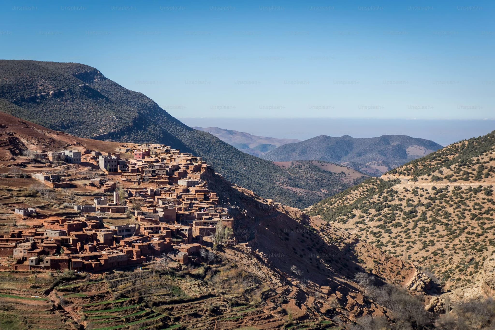 A rustic village with clay and stone houses nestled on a hillside under a clear blue sky. Surrounding mountains create a peaceful, remote atmosphere.
