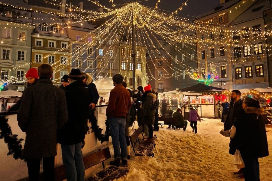 A festive evening shot of a brightly lit Christmas market in a snowy historic square.