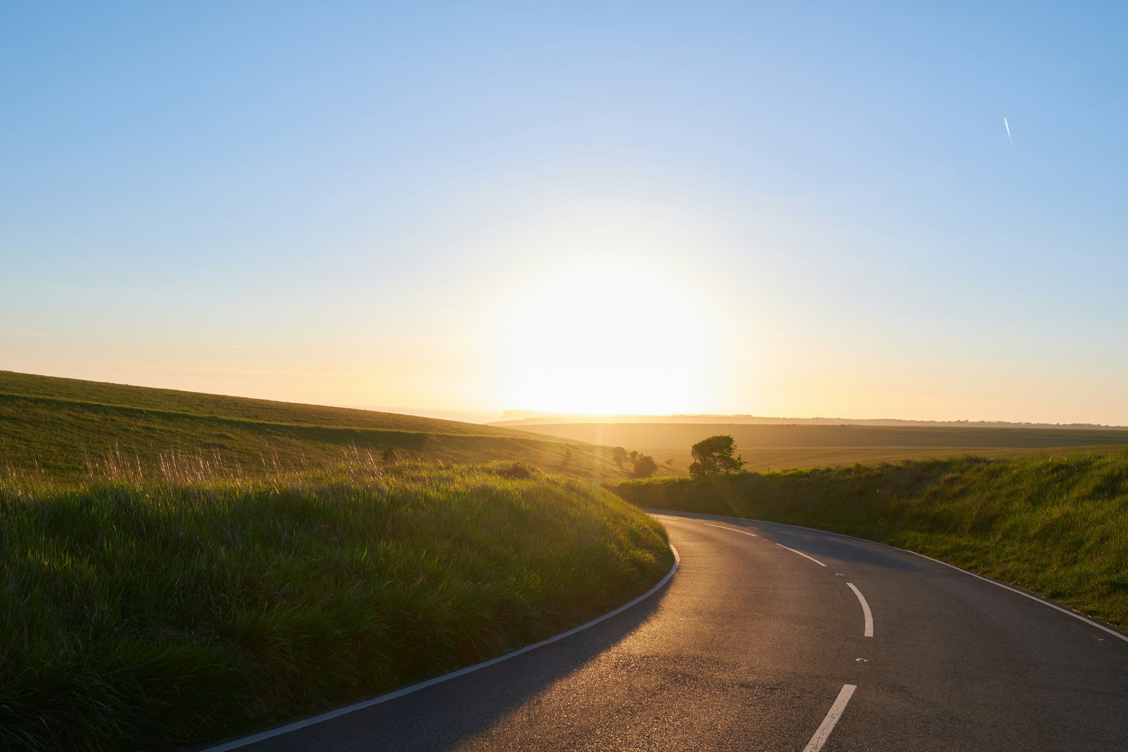 Empty road in green landscape at sunrise
