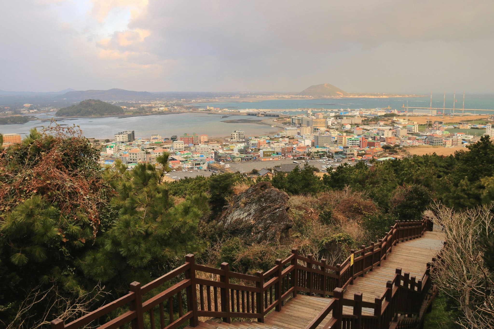 A wooden staircase on a green hill and tiny houses and ocean and island in the background