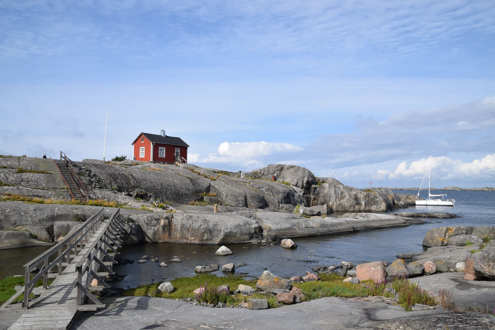 Red wooden house on top of rocky area near the water connexted by a wooden bridge