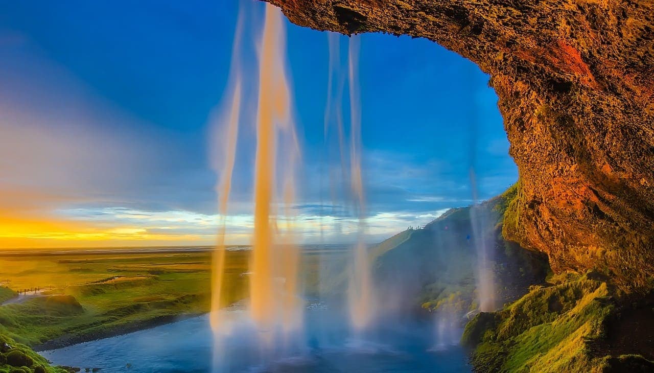 Seljalandsfoss waterfall viewed from behind the falling water at sunset with golden light over the landscape.