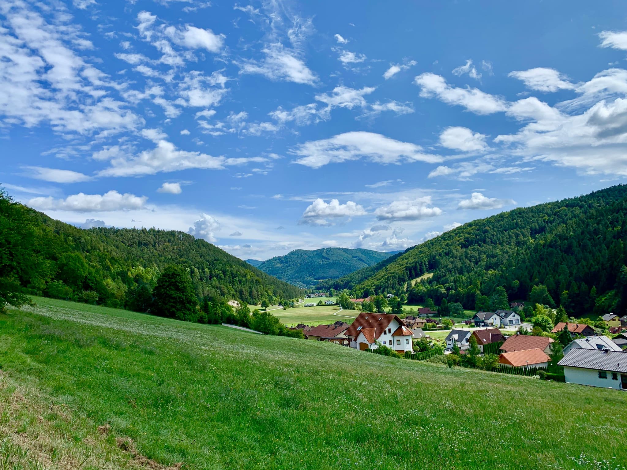 A green grass hill surrounded by mountains and tiny houses in a village in Austria