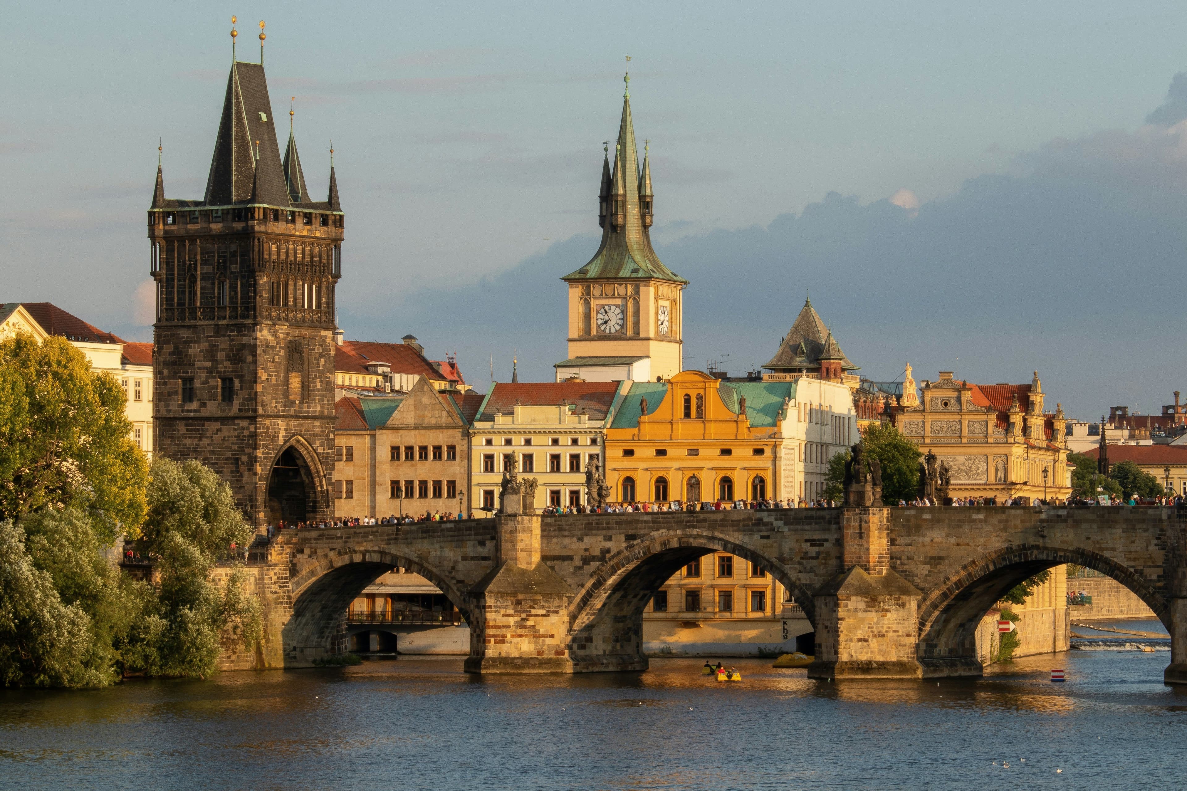 The bridge of Prague on the river of Prague, with the tower of the bridge on the left and houses buildings in the background