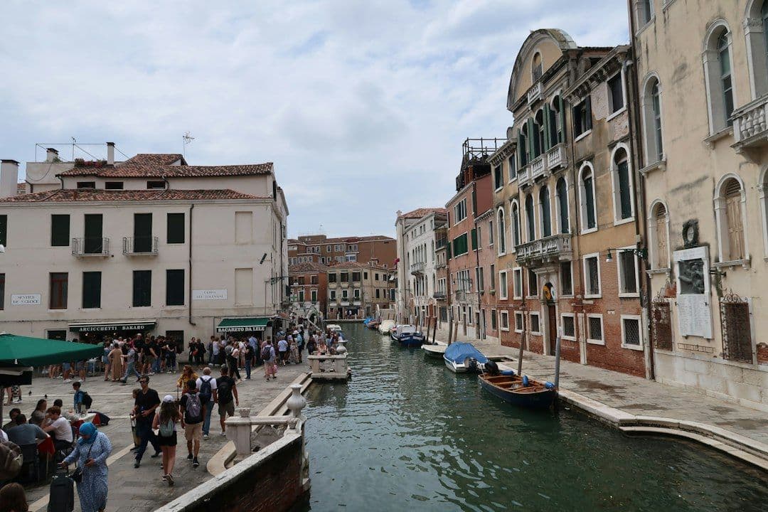 Historic buildings line a crowded Venice canal with boats and people