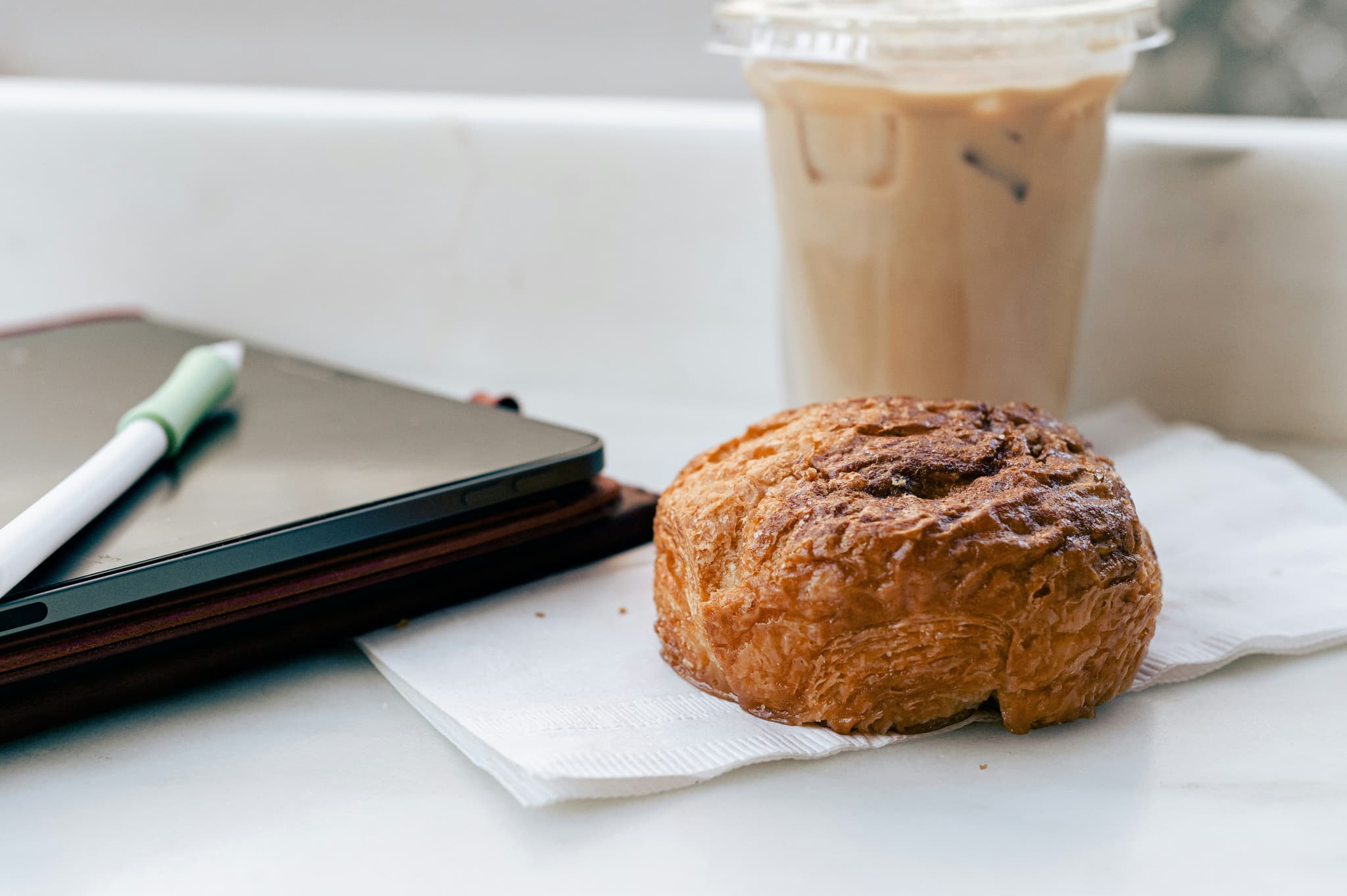 Kouign-amann pastry on a desk next to a cup of iced coffee