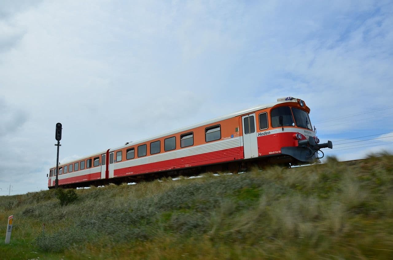 A red and white train travelling through open countryside under a cloudy sky, representing rail travel across Europe
