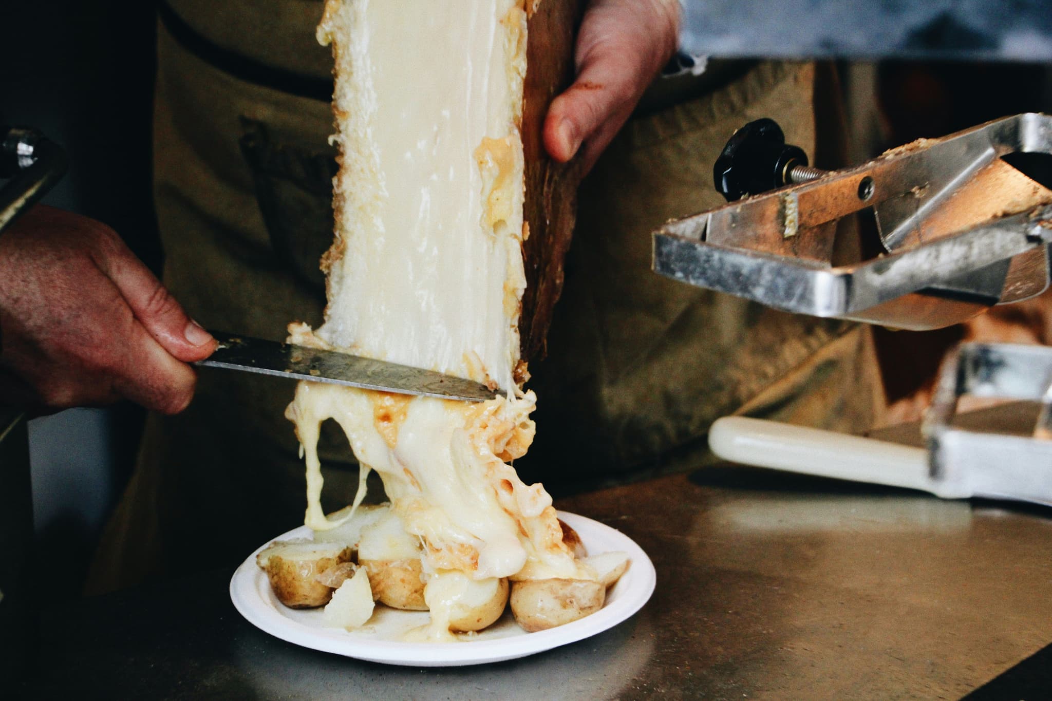 Raclette cheese being scraped over boiled potatoes
