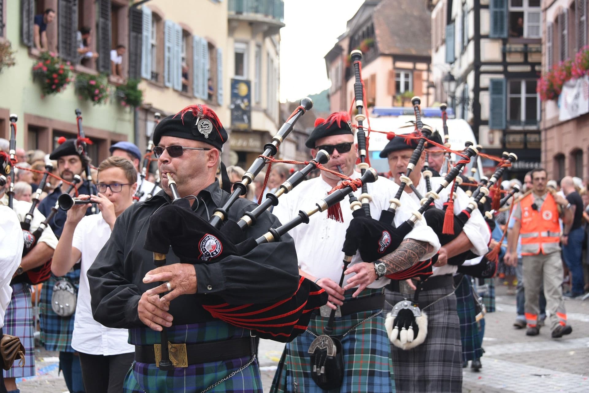 A group of men playing local instrument, wearing kilts in scotland in a crowd.