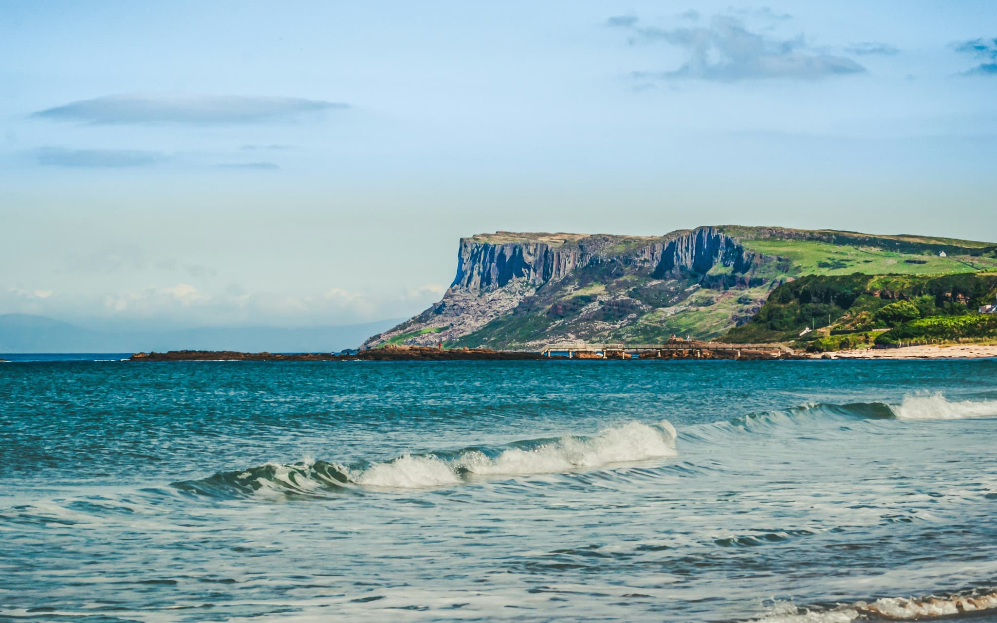 Cliffs with greenery and blue sea with waves at Ballycastle Beach