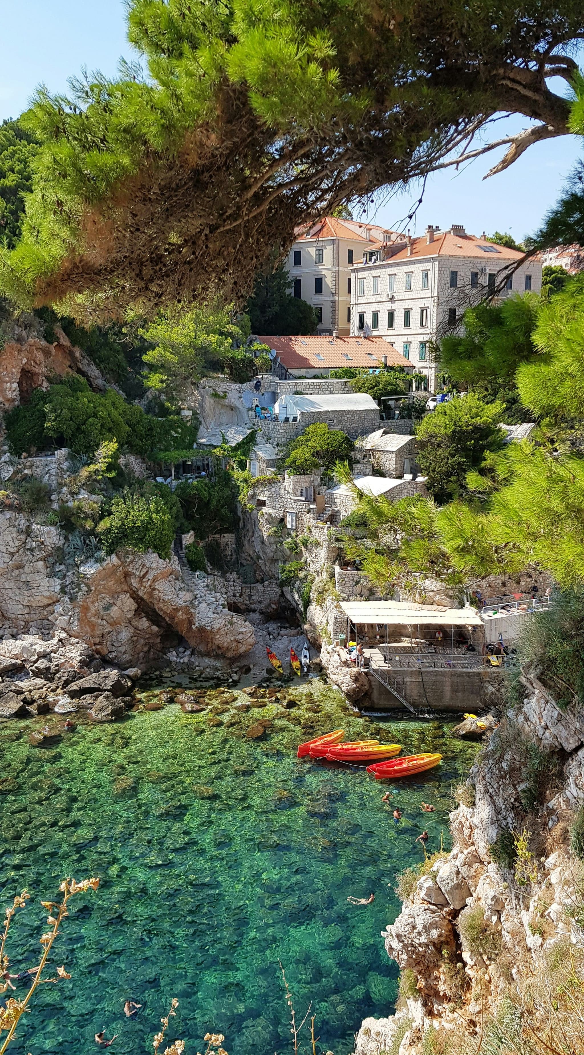 Orange kayaks in a clear cove below stone buildings in Dubrovnik