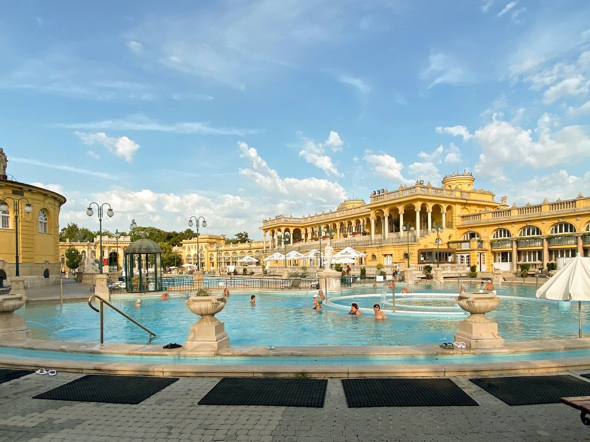 People walking outside the Széchenyi Thermal Baths in Budapest on a summer morning