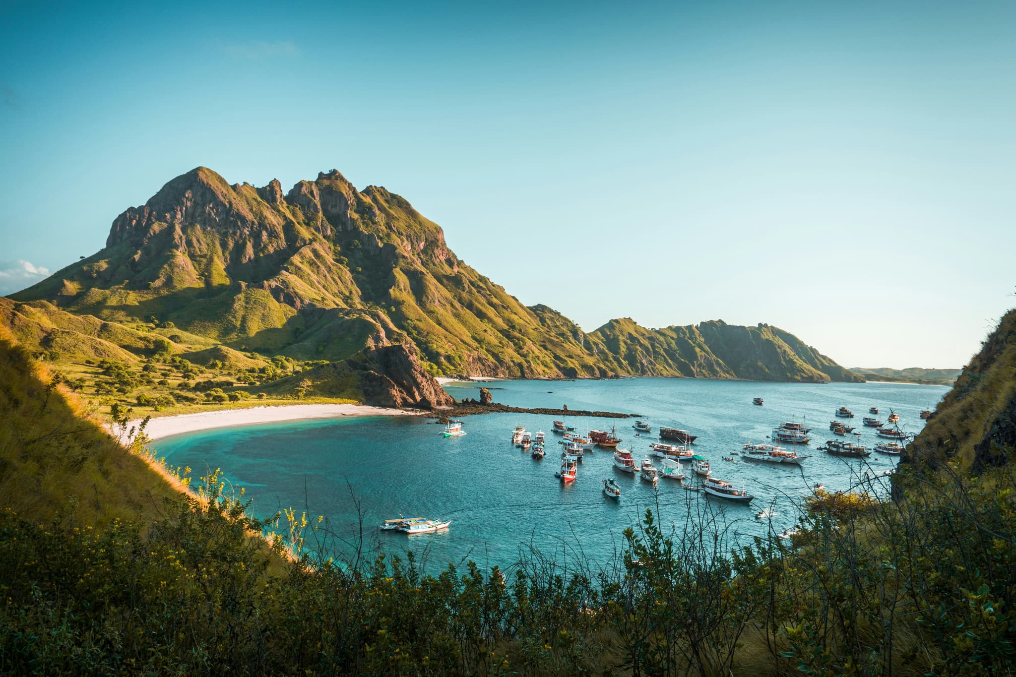Bay of Komodo from above, clear blue water with boats and mountains surrounding it