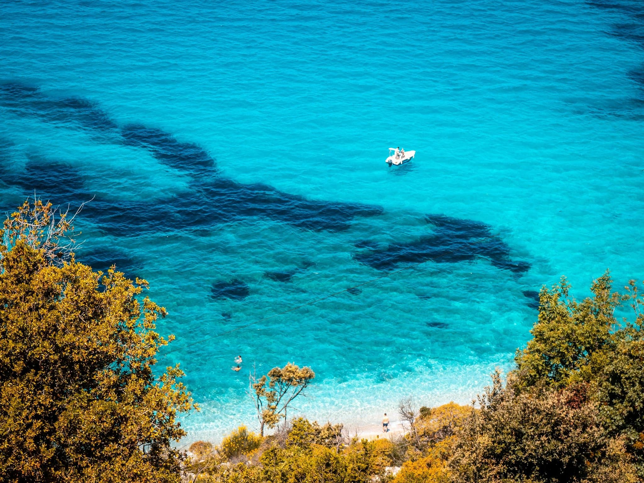 A small boat on clear turquoise water by a green shore