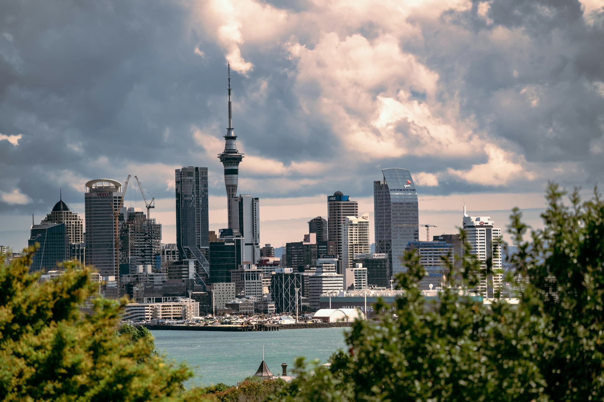 City skyline of Auckland by the river surrounded by trees on a cloudy day