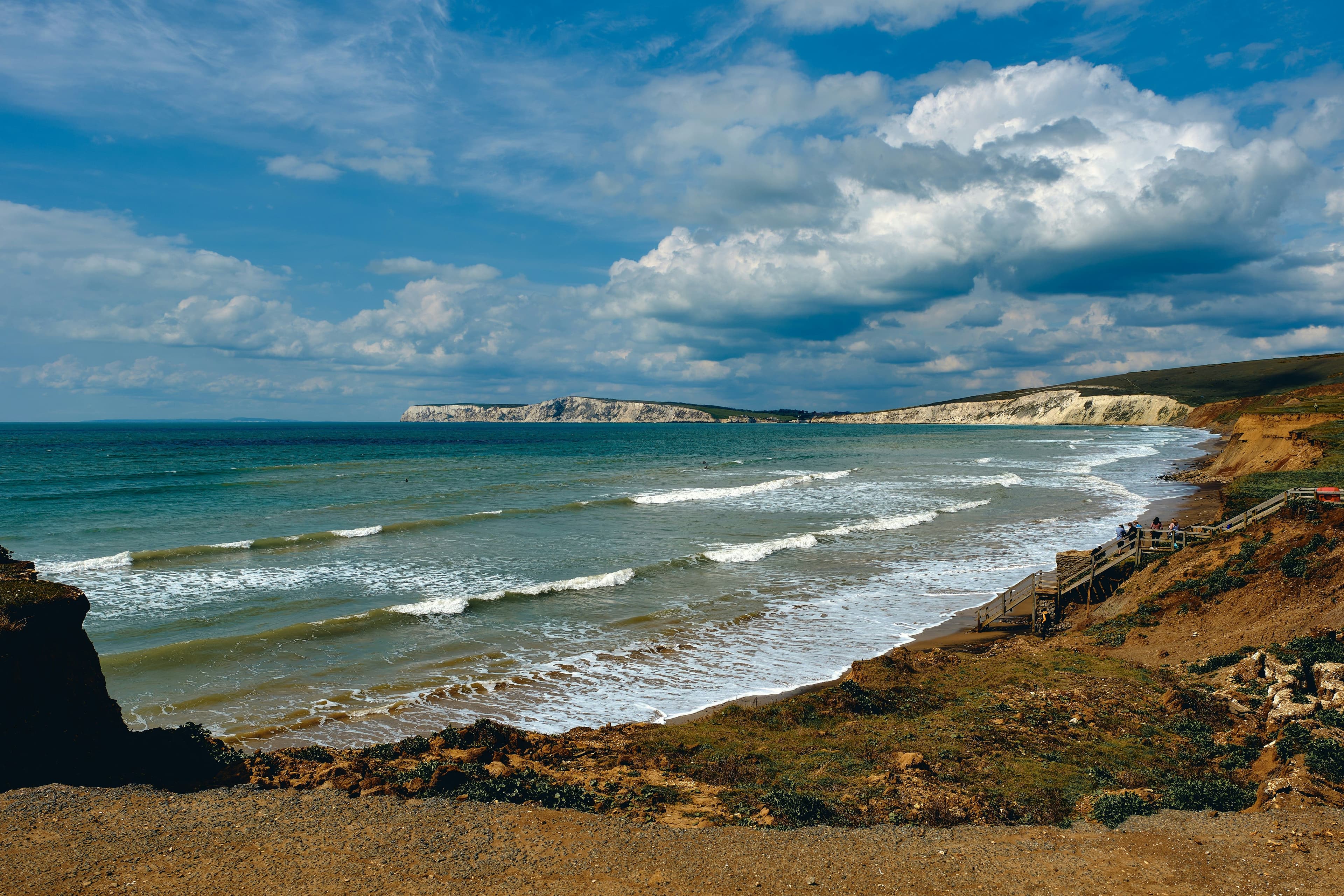 Beach with rock formations on the right and the ocean on the left. It is a cloudy day with blue sky.