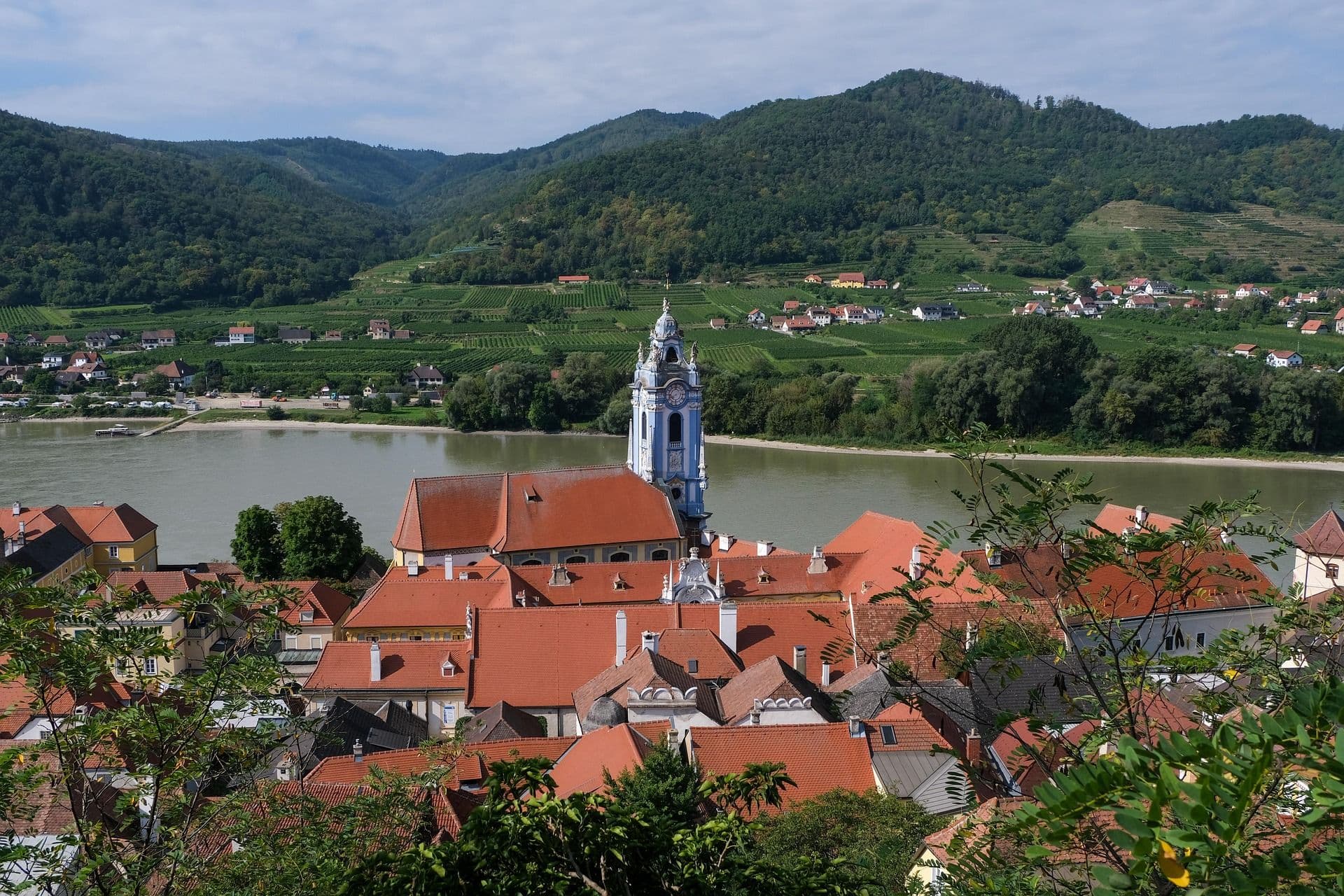 Red colorful roofs and a church by the water in Wachau Valley surrounded by green mountains