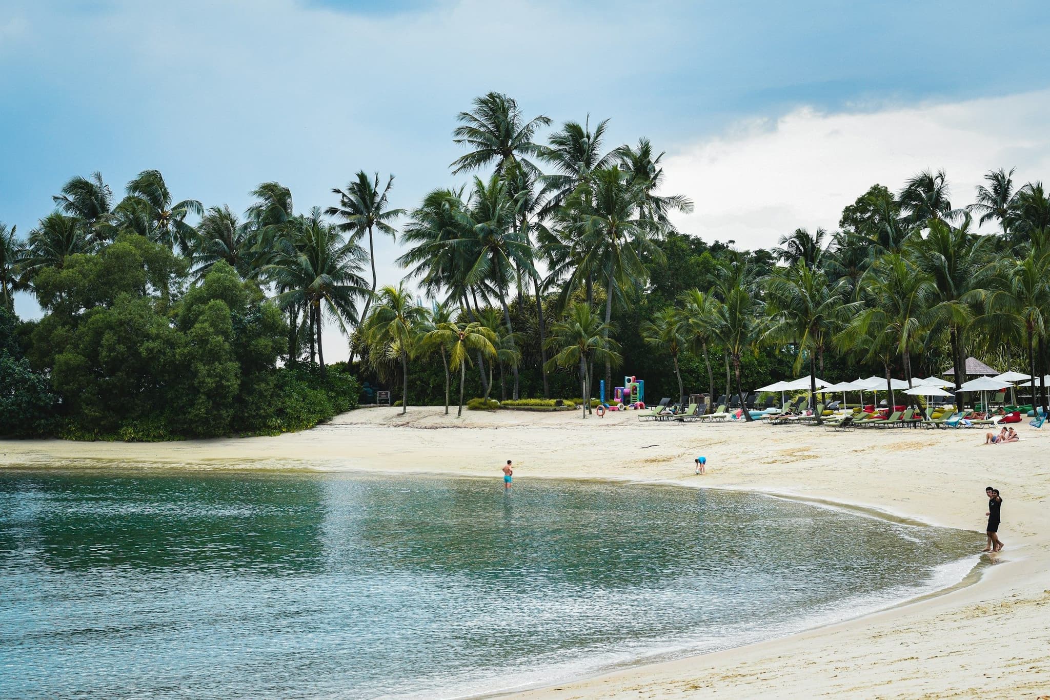 A sandy beach with palm trees and umbrellas on Sentosa