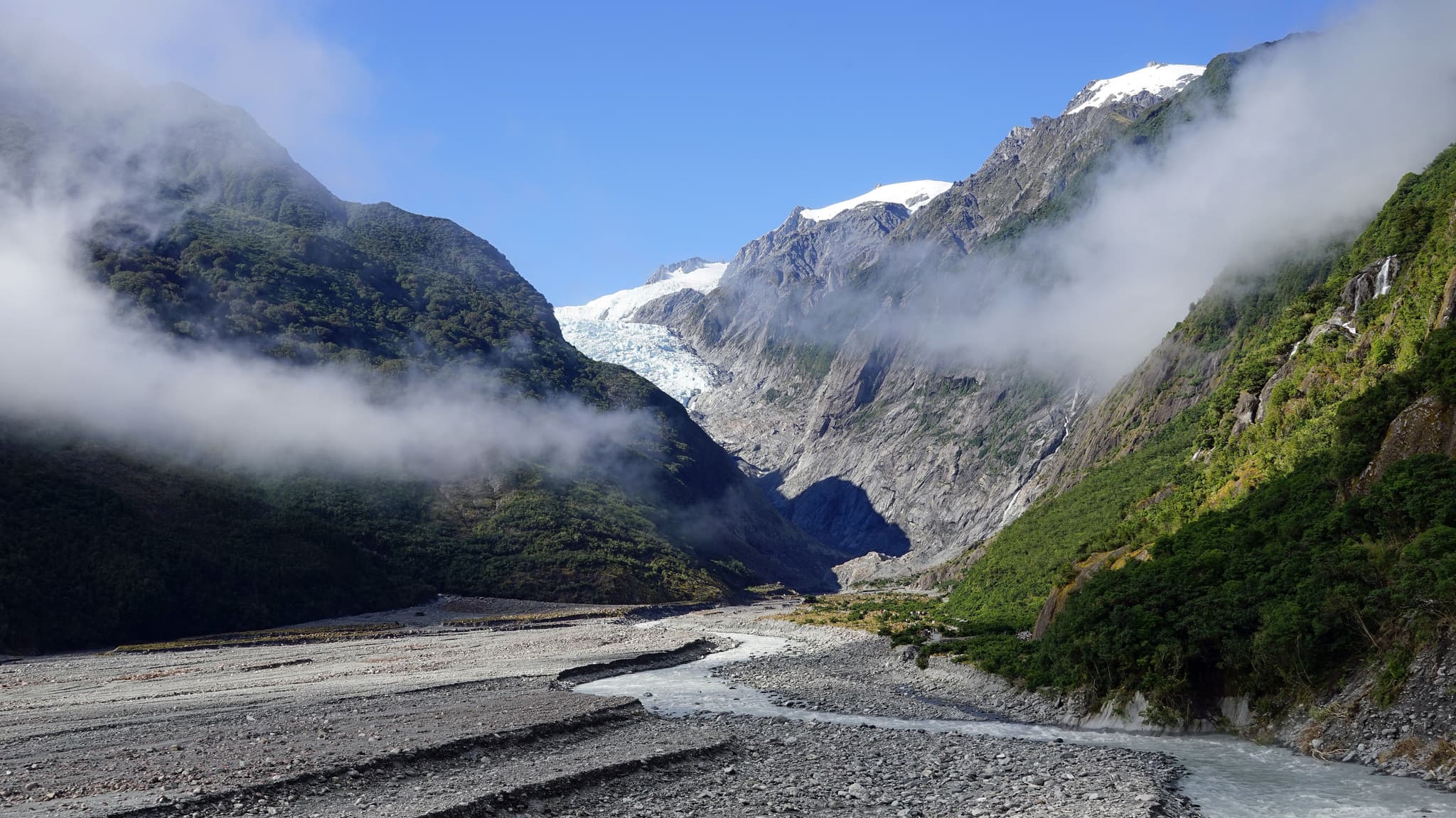 Franz Josef Glacier valley New Zealand with steam clouds and green rocky mountains