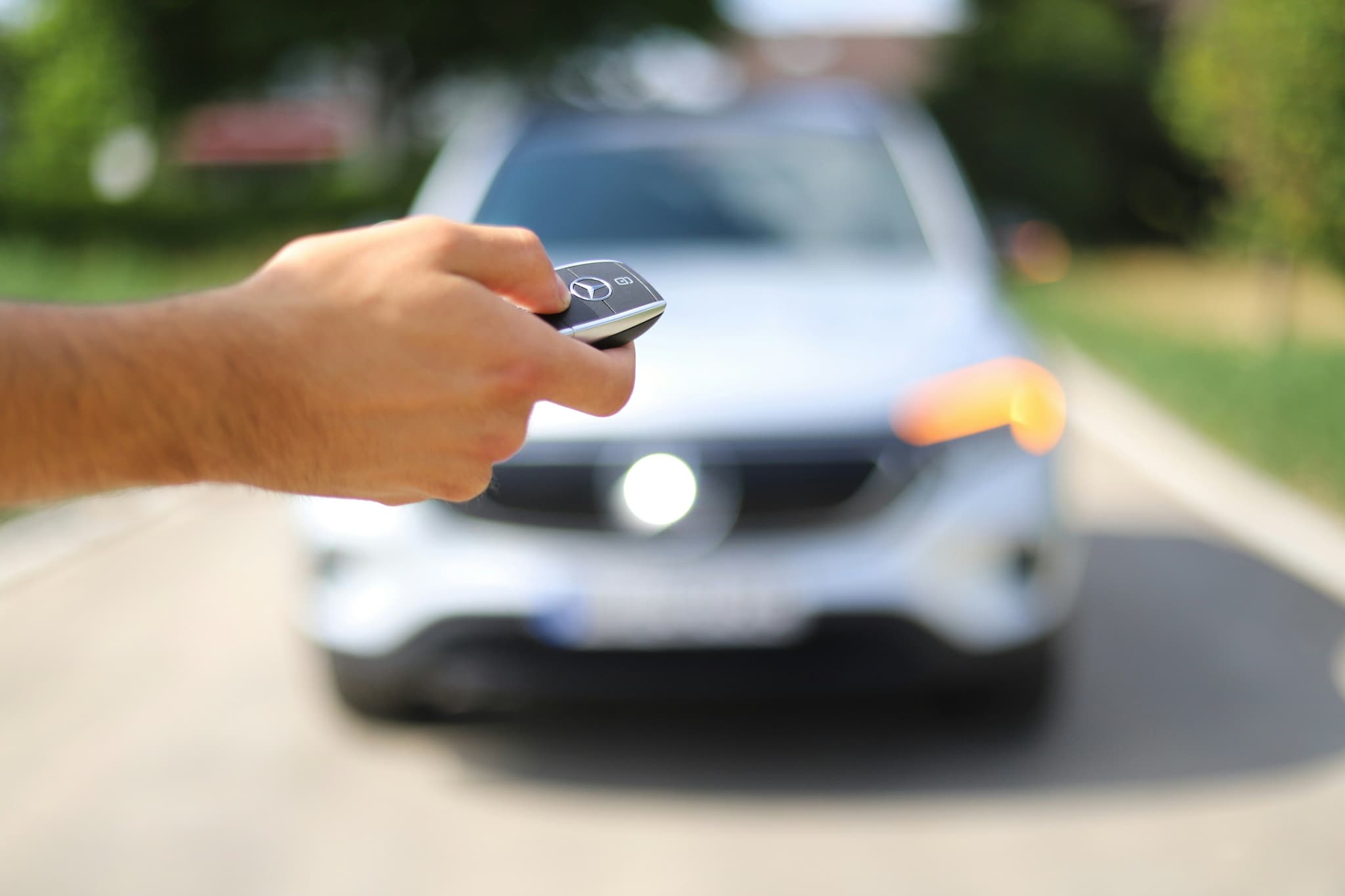 A hand holding a car key, car blurred in background