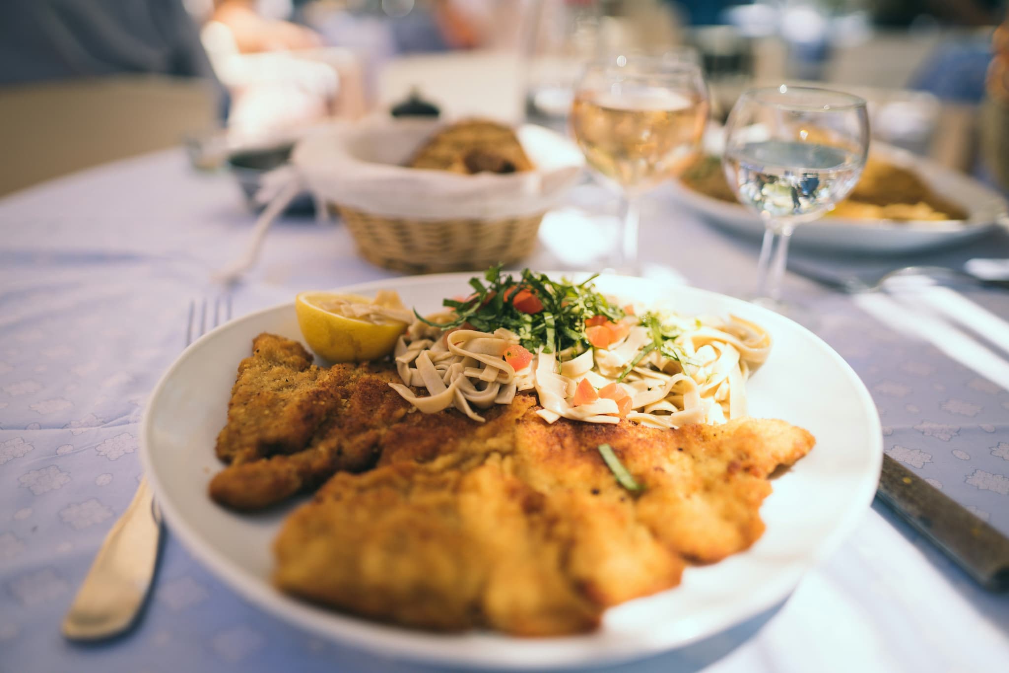 A schnitzel on a white plate with wine glasses
