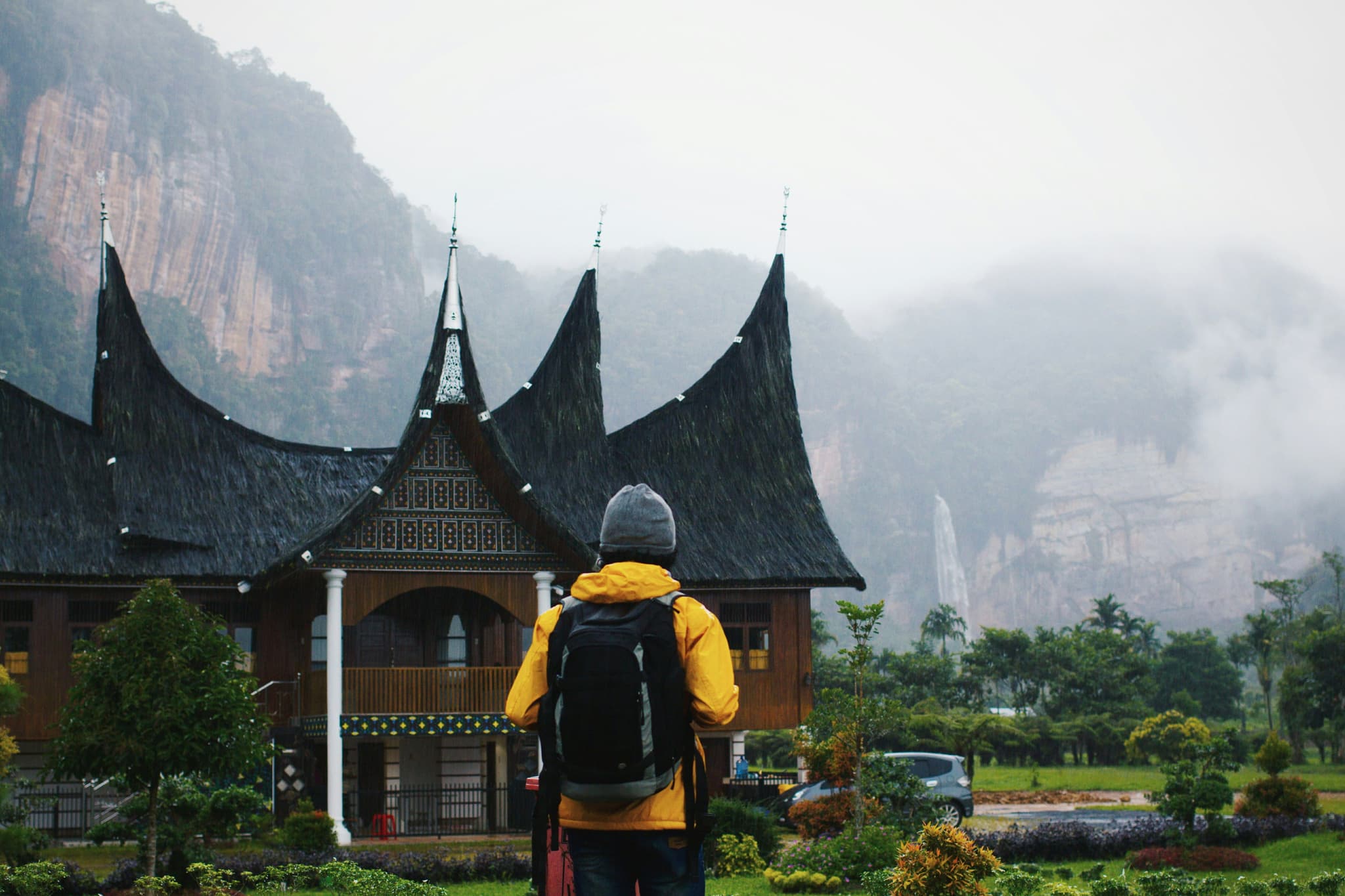 Solo traveller with small backpack hiking toward a temple surrounded by limestone cliffs and mist