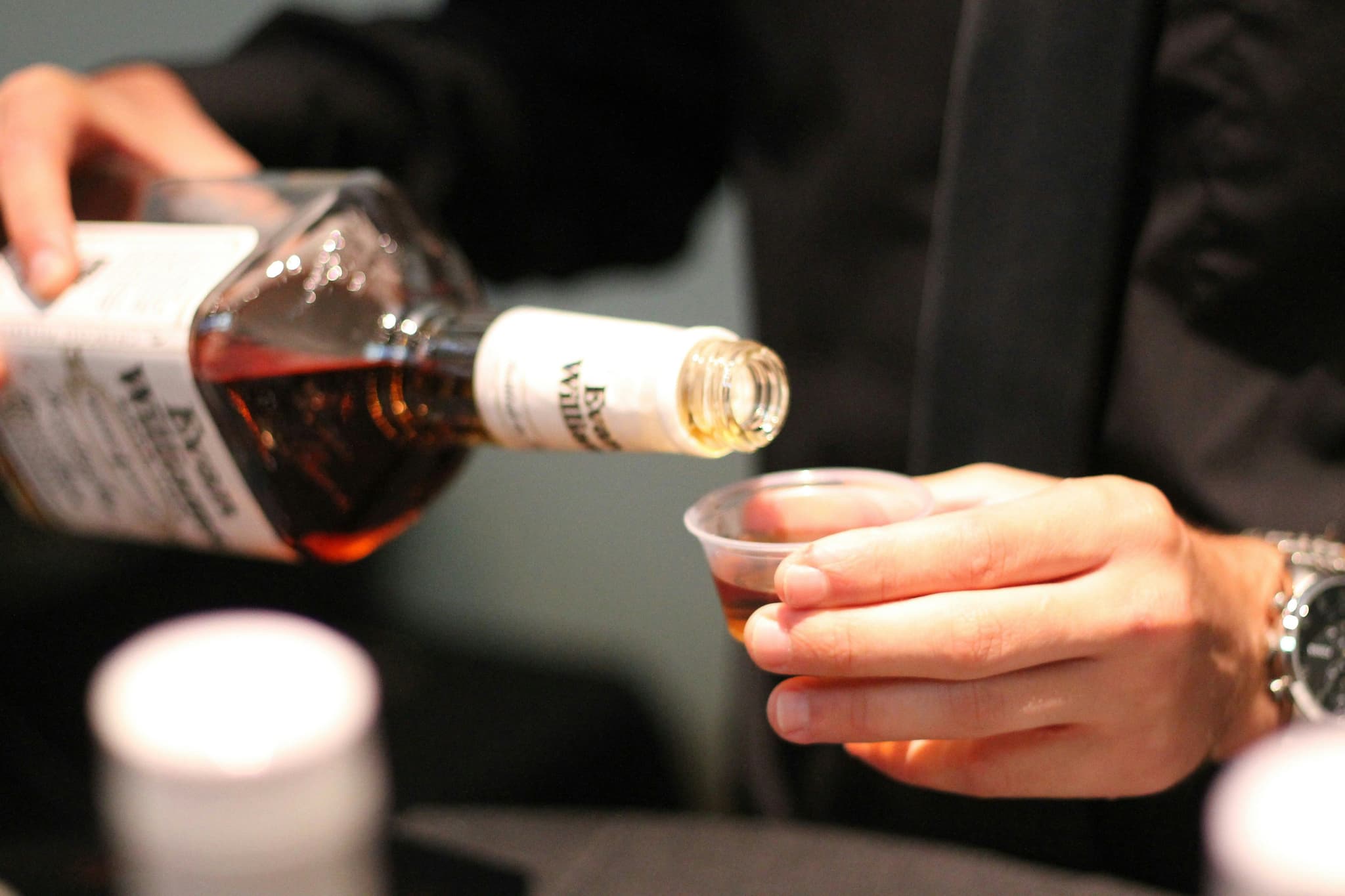Hand pouring wiskey from a bottle into a small test cup