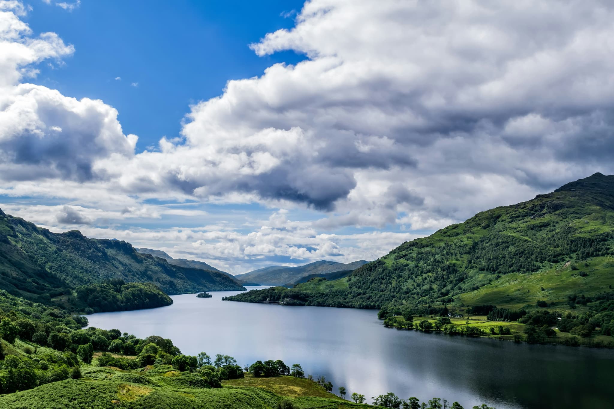 Mountanous landscape green grass and lake with clouds in the air in Loch Lomond