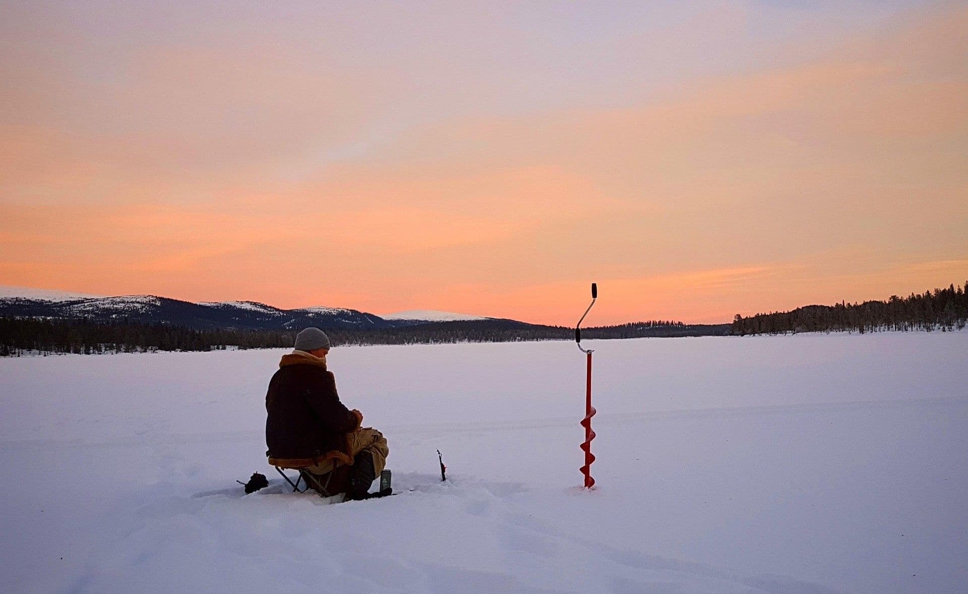 man sitting on ice during an ice fishing activity at sunrise